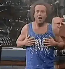 David Spade singing with hand on chest