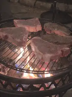 Raw steaks grilling over open fire
