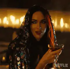 Megan Fox holding a drink in a sequin hood