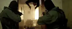 Bald man hanging upside down with guns