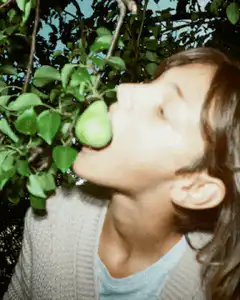 Person biting a pear on a tree