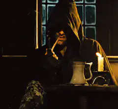 Hooded figure smoking by candlelight