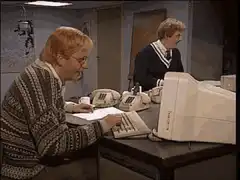 Two men laughing at a desk with phones