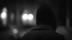 hooded figure exhaling smoke at night