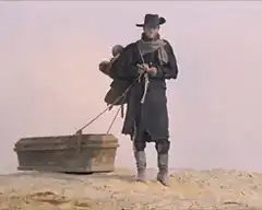 Man pulling coffin in desert
