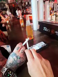 Tattooed hands holding cigarettes at a bar