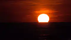 Bright sun setting over dark ocean