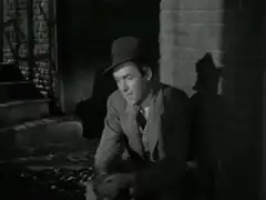 Man in fedora sitting by brick wall