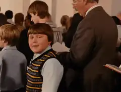 Boy in sweater vest smiles and looks around