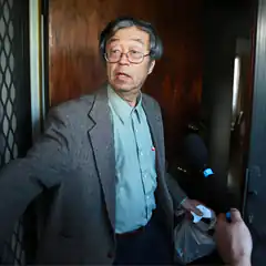 Man in glasses holding plastic bag talking to reporter