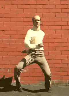 bald man dancing against brick wall