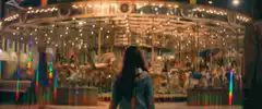 Woman watching a lit carousel at night