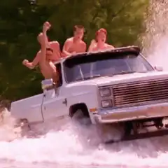 Shirtless men cheering in a truck driving through water