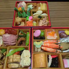 Three red bento boxes with assorted Japanese food