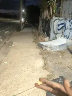 hand holding yellow object on sidewalk at night