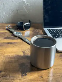 Coffee cup on wooden desk with laptop and watches