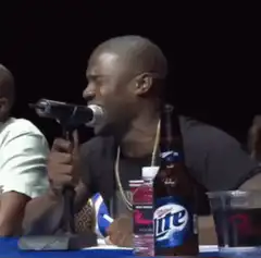 Kevin Hart laughing into a beer bottle