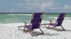 Two purple beach chairs on white sand