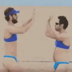 Two men in bikinis high five on beach