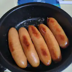 Five sausages frying in a pan