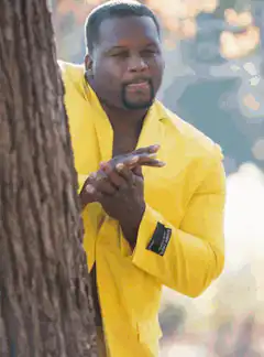 Man in yellow and pink suit peeking from behind tree