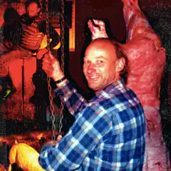 Man in plaid shirt pulling chain next to meat