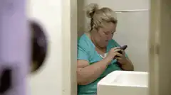 woman using phone in bathroom stall