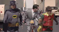 Batman and Robin walking with Commissioner Gordon on a bike