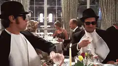 Two men in tuxedos and sunglasses clinking glasses