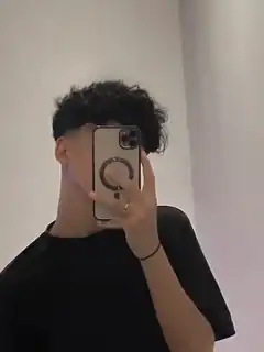 curly-haired person taking mirror selfie