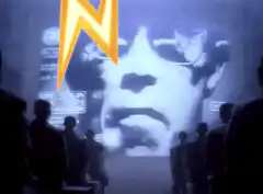 Silhouettes watching a giant face on a screen