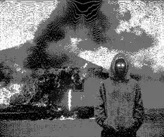 Hooded figure standing in front of a burning house