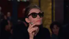 Audrey Hepburn smoking and looking over sunglasses