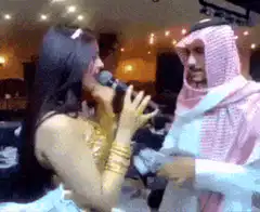 Woman singing into microphone with man in thobe