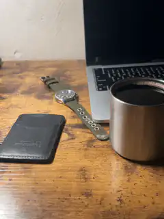 laptop, watch, wallet, and coffee cup on wooden desk