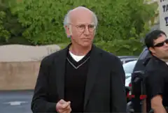 Larry David walking and grimacing