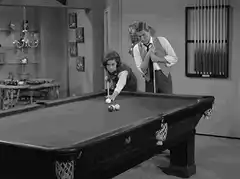 Woman plays pool while man watches