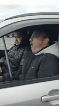 Two men in a car singing and dancing