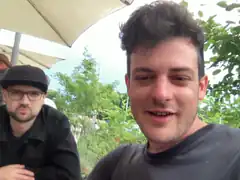 Two men sitting outside under an umbrella