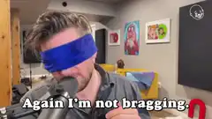 Man blindfolded with blue cloth speaking into microphone