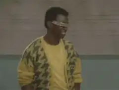 Man in yellow cardigan and glasses gives thumbs up