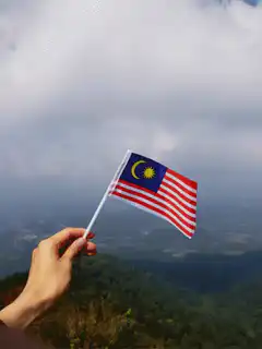 Hand holding Malaysian flag on mountain