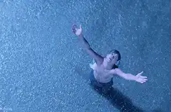 Man standing in heavy rain with arms outstretched