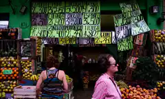 woman walking past fruit stand with price signs