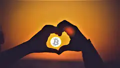 hands forming heart around bitcoin