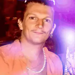 Man in pink shirt and pearls smiling