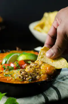 Hand dipping tortilla chip into cheesy dip