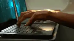 Two people typing on laptops with code