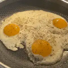 Three fried eggs cooking in a pan