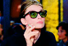 Audrey Hepburn smoking and lifting sunglasses